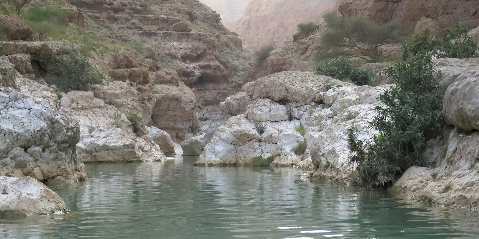 Türkisfarbener Pool zwischen rostroten Schluchtwänden bei Wadi Shab, Oman