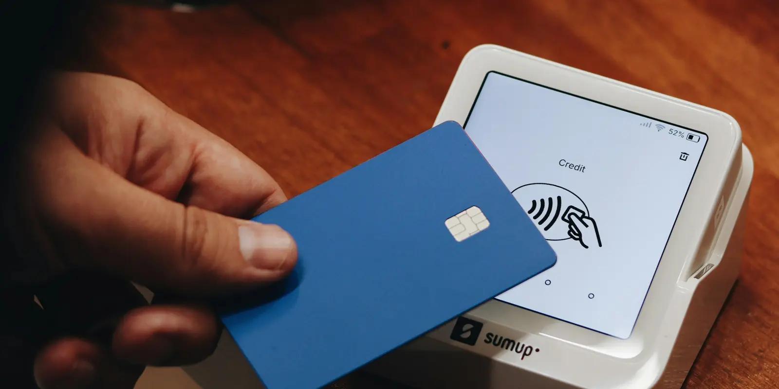A hand holding a payment card next to a smartphone, illustrating the billing question behind an eSIM purchase