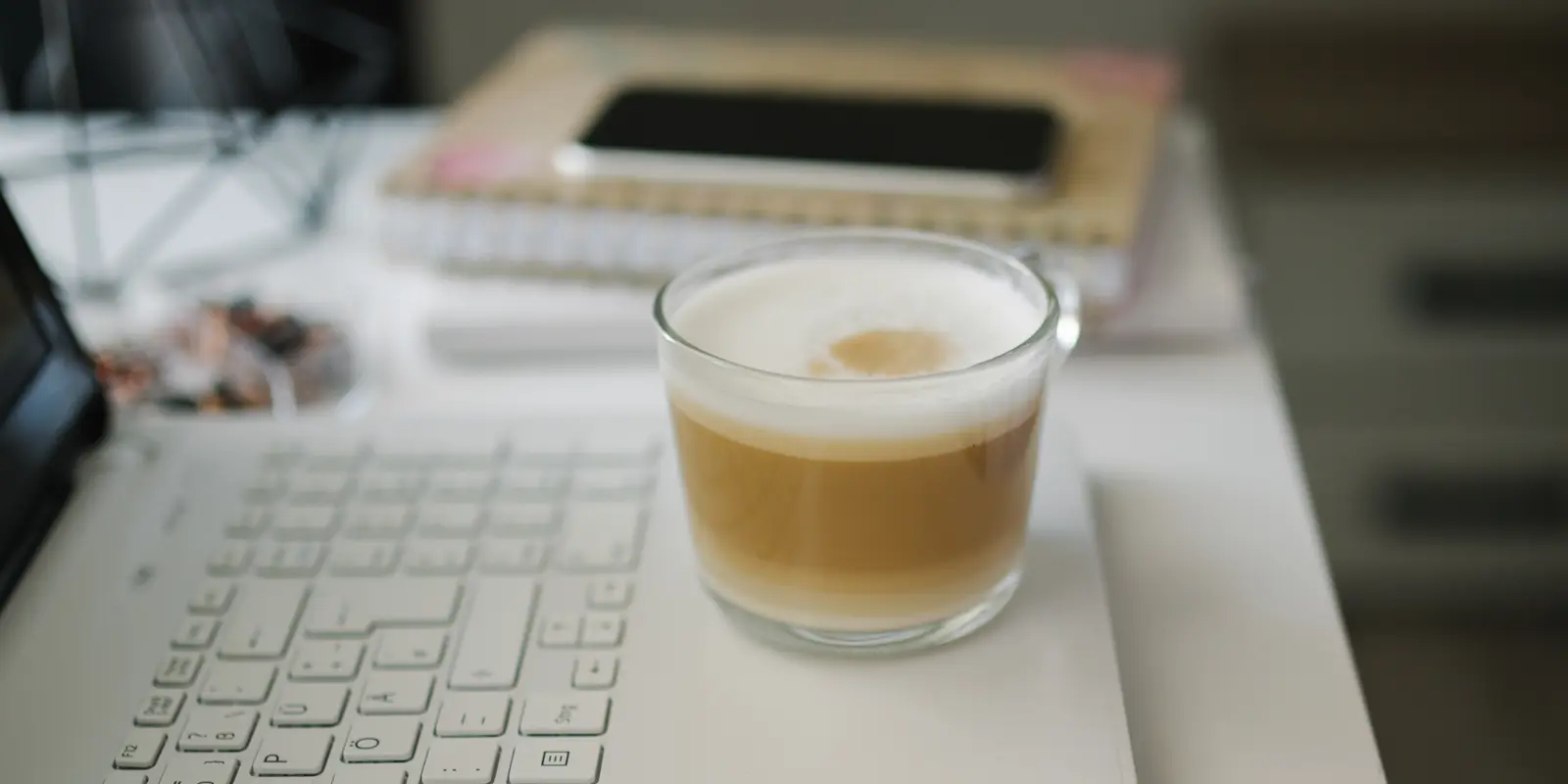 Ein Smartphone liegt auf einem Notizbuch neben einem Laptop und Kaffee.