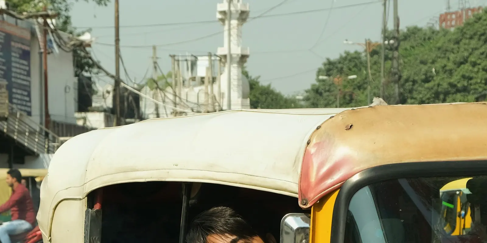 A man using his phone while riding in an auto rickshaw on a New Delhi street, illustrating everyday connectivity needs for tourists in India