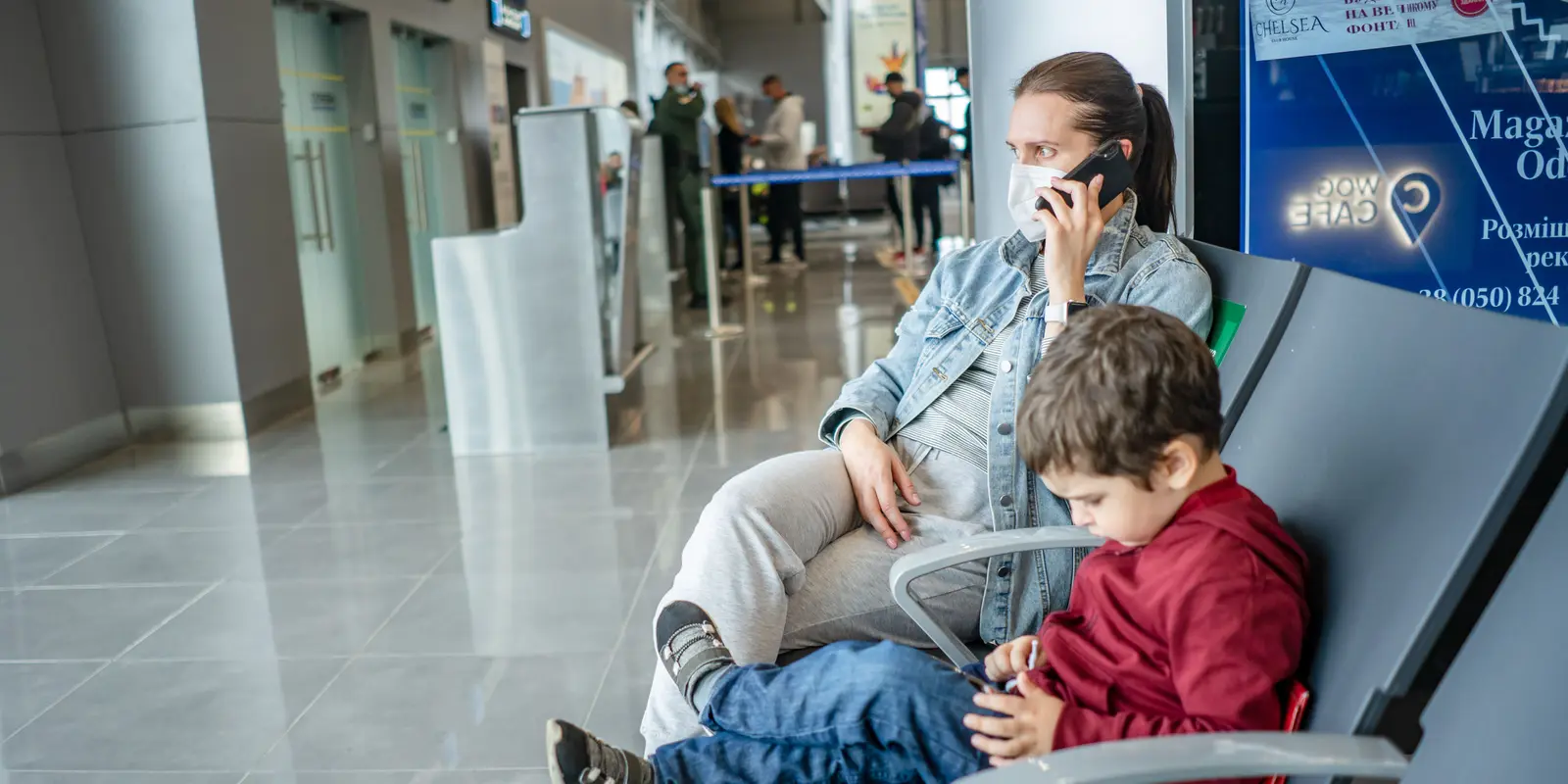 Eine Mutter und ihr Kind nutzen getrennte Geräte während sie am Flughafen warten