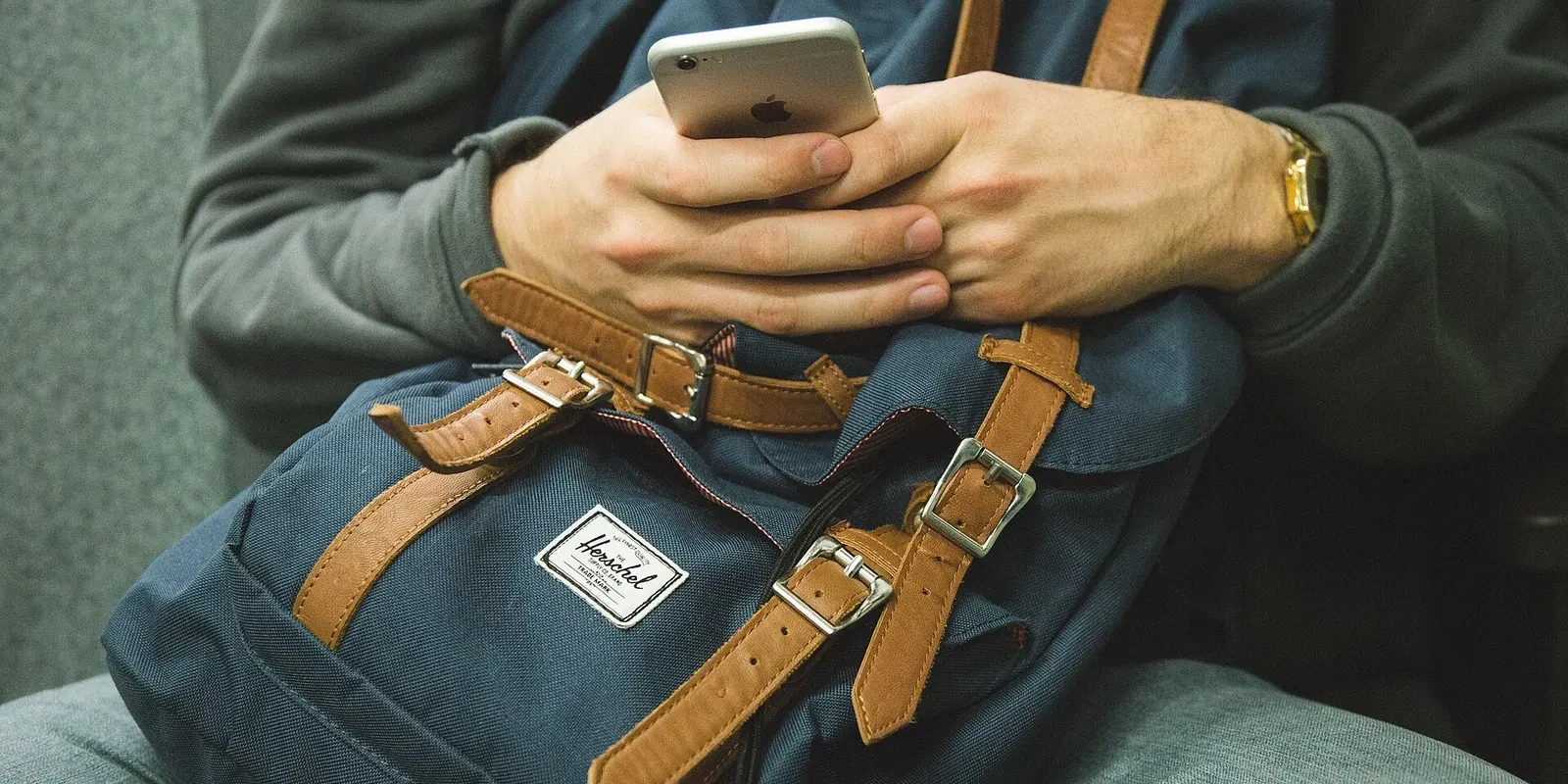 Eine sitzende Person hält ein Smartphone über einem Rucksack auf dem Schoß.